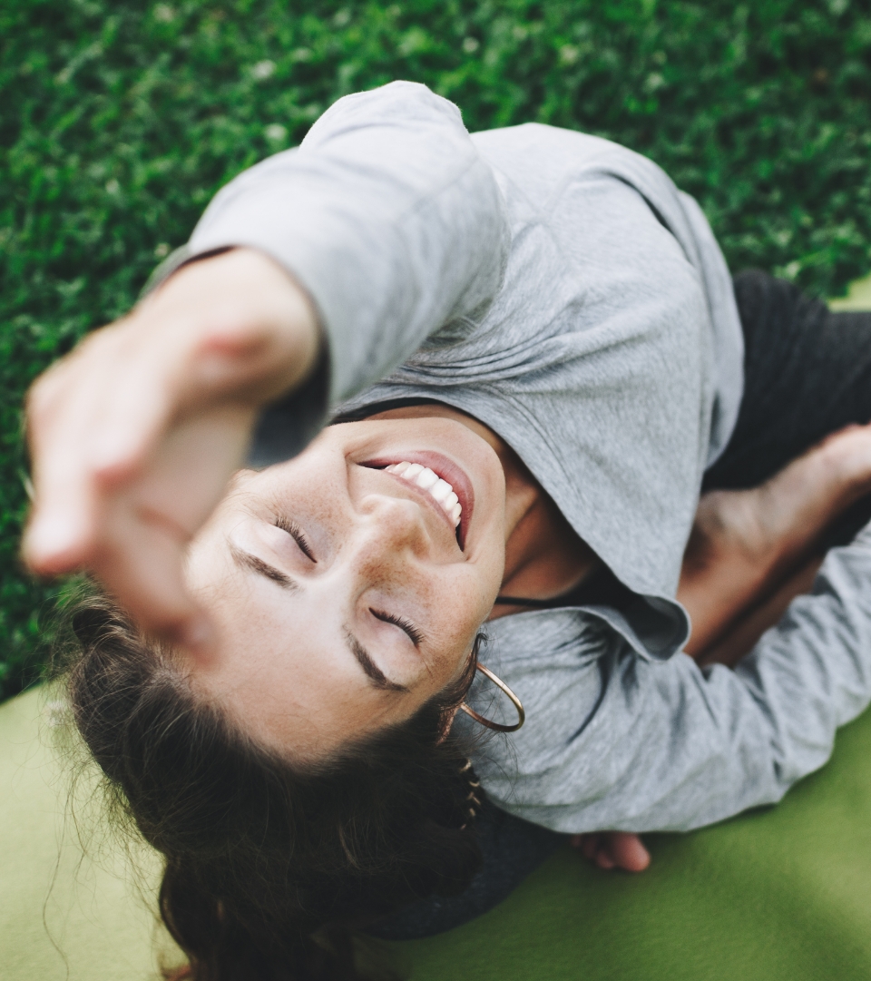 Seen from above, a smiling woman reaches up while doing a yoga pose.