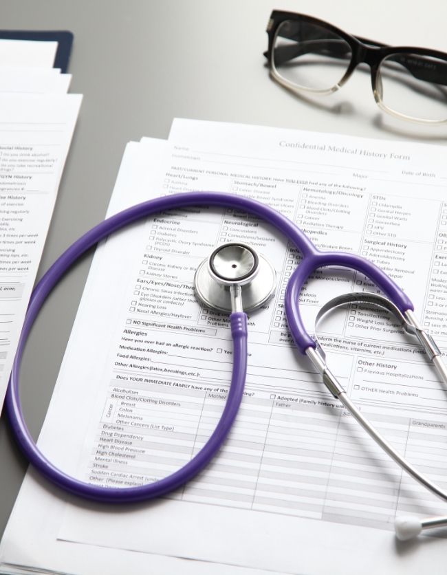 A photo of documents laid out on a desk with a stethoscope and pair of glasses nearby.